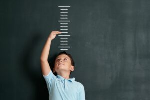 Child in front of lines on a blackboard to measure his height with an arm up to his future growth