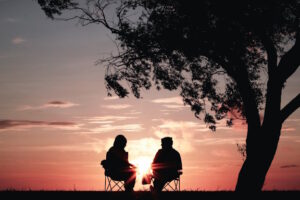Silhouette of two people sitting underneath a tree looking at the sunset
