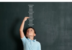 Boy in front of lines blackboard to measure his height with an arm overhead to show his future growth
