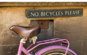 Pink bicycle resting against a wall where a sign says :no bicycles please"