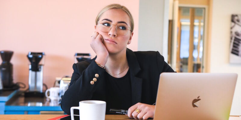 Bored woman sitting at computer, chin on her had looking away from screen