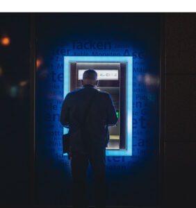 Man at ATM machine at night with blue lights surrougding the ATM